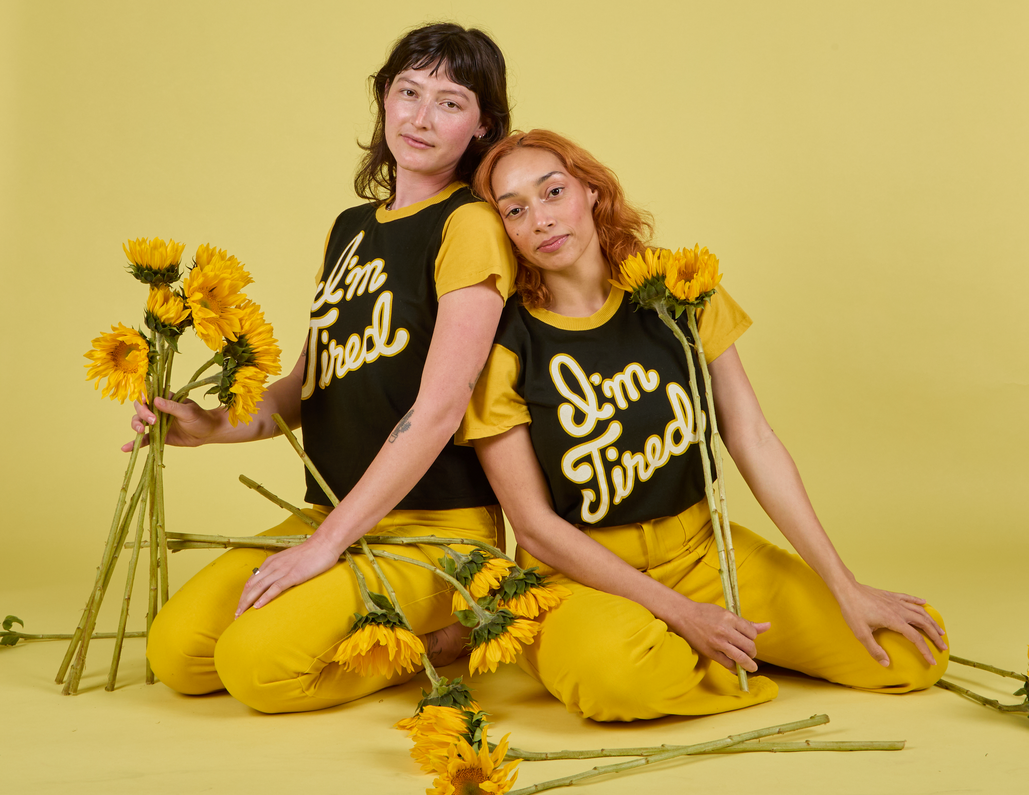 Alex and Tiara are both wearing the I'm Tired Anniversary Tee paired with Work Pants in Golden Yellow.