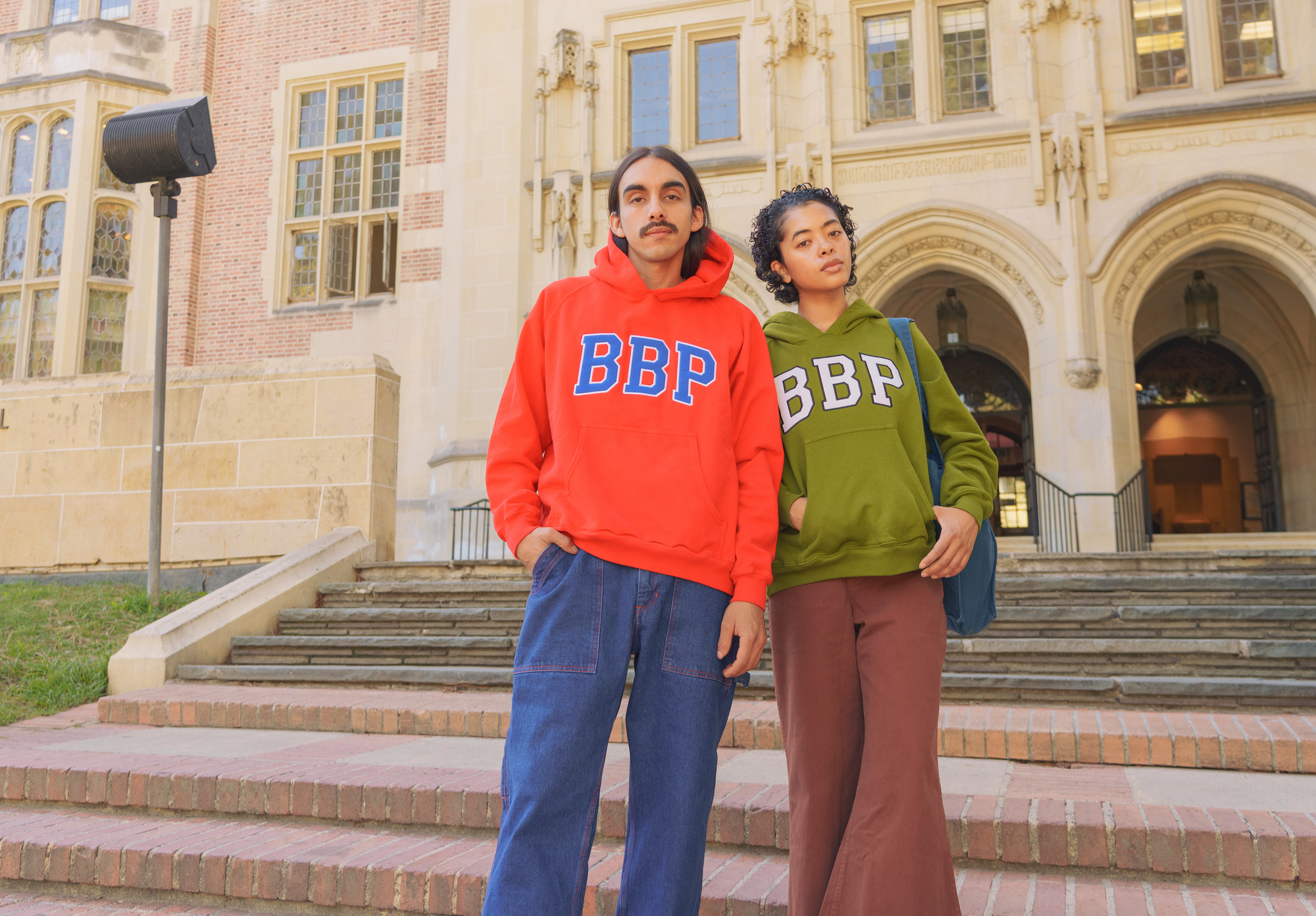Mika is wearing the Collegiate Hoodie in Mustang Red paired with Bell Bottoms in Fudgesicle Brown.  Anthony is wearing Collegiate Hoodie in Summer Olive paired with Carpenter Jeans in Dark Wash