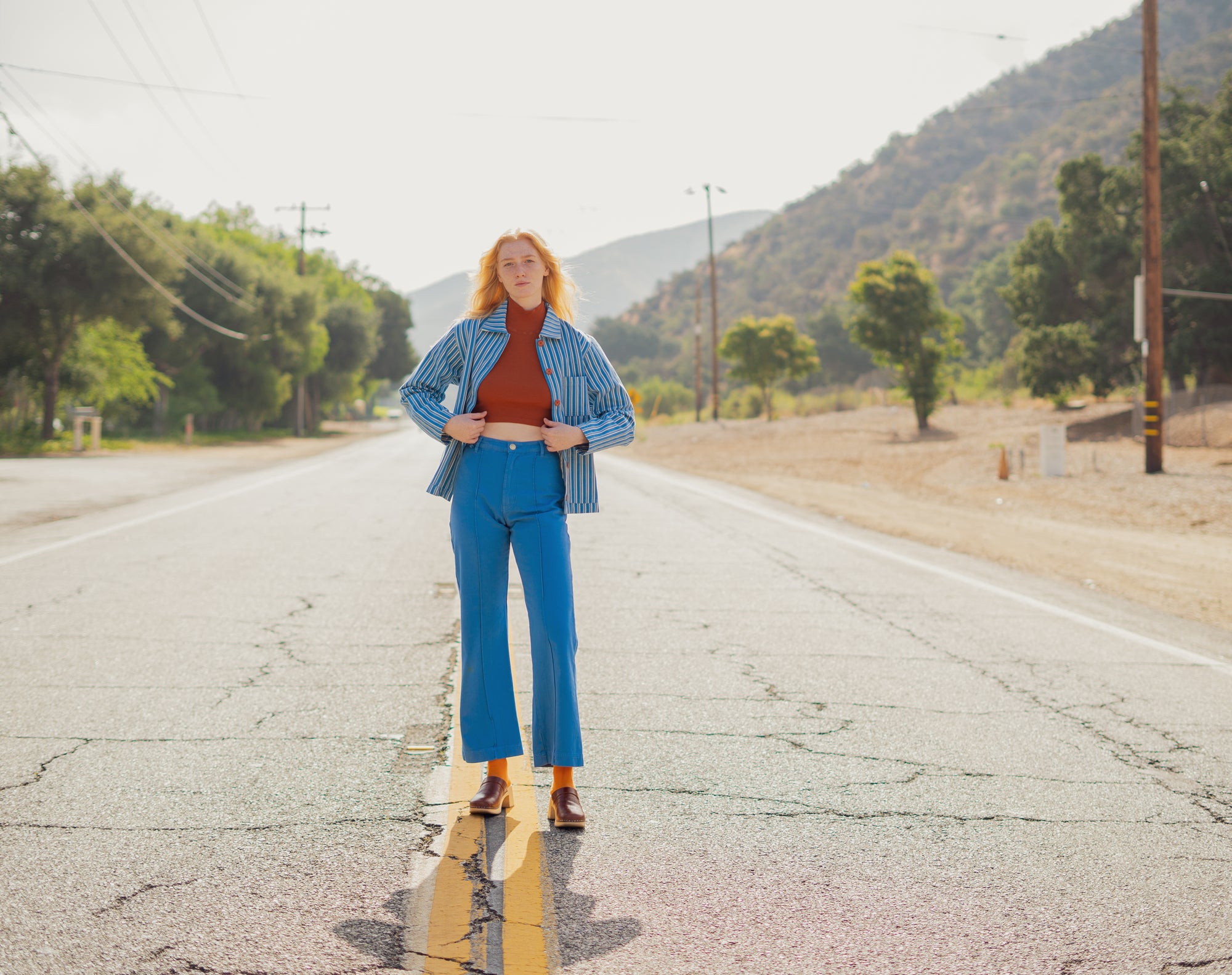 Margaret wearing Frontier Stripe Work Jacket in Blue, Sleeveless Essential Turtleneck in Burnt Terracotta, Western Pants in Greek Blue, and Everyday Socks in Spicy Mustard
