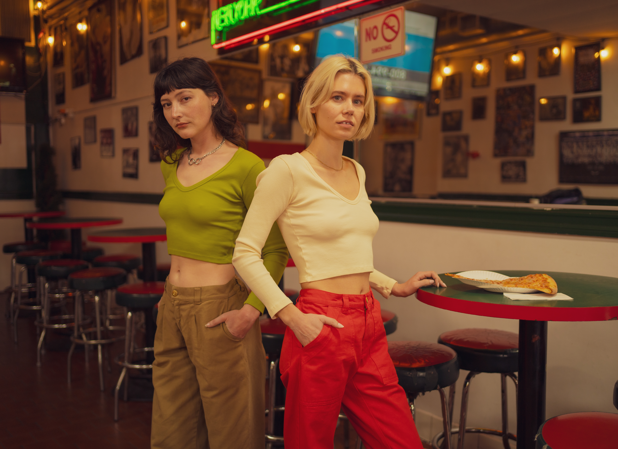 Alexandra Skye is wearing a Long Sleeve V-Neck Tee in Gross Green paired with Mid-Rise Pleated Trousers in Desert Brown. Madeline is wearing Mid-Rise Work Pants in Mustang Red