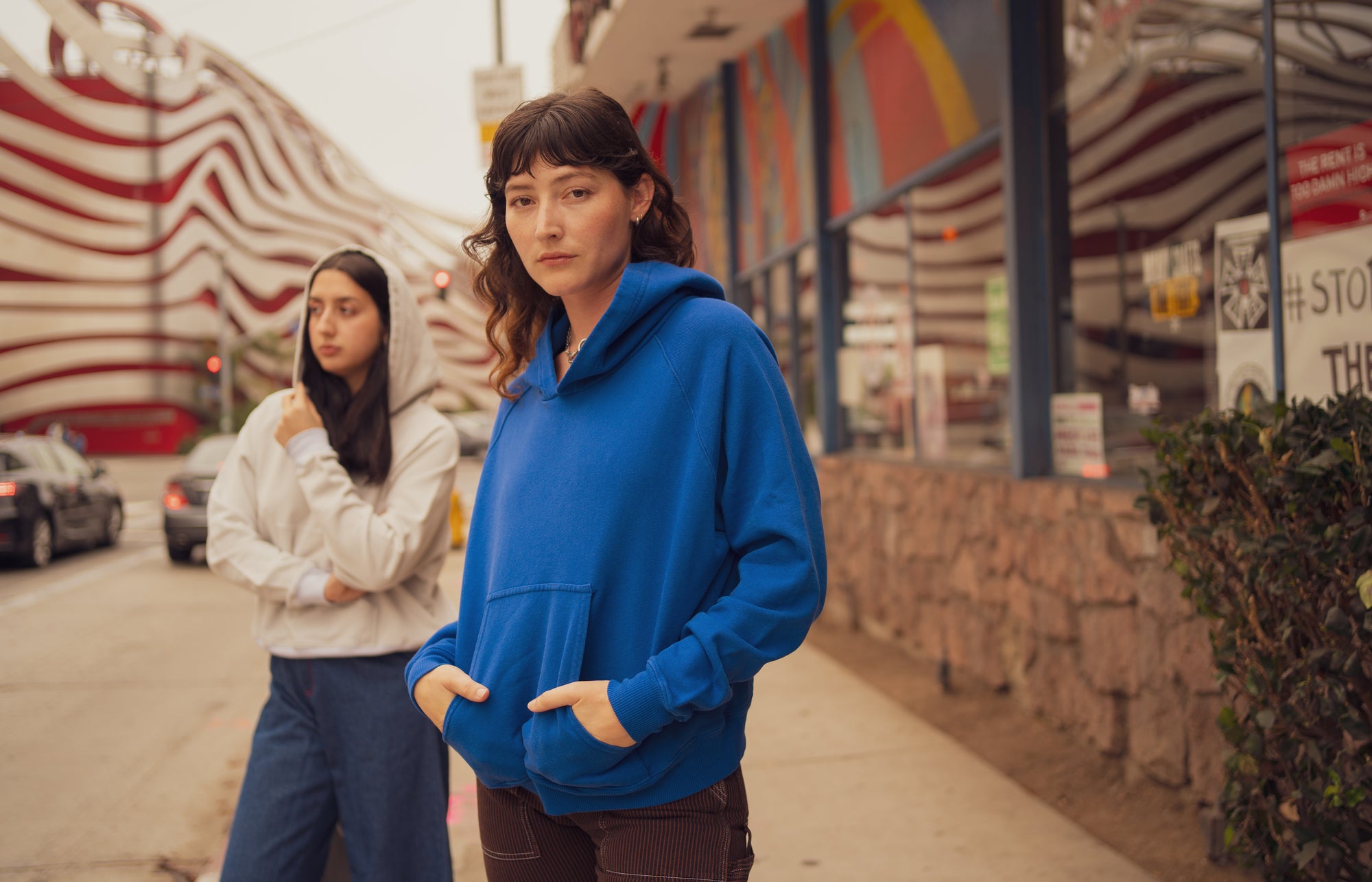 Alexandra Skye is wearing Oversized Hoodie in Royal Blue and Railroad Carpenter Jeans in Fudgesicle brown. Betty is wearing Oversized Hoodie in Dishwater White paired with Indigo Wide Leg Trousers in Dark Wash.