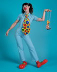 Alex is wearing a short sleeve jumpsuit in baby blue with a red clown nose, red clown shoes and a large polka dot tie