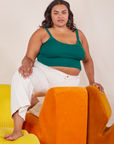 Alicia is kneeling on an orange upholstered chair with one foot on a yellow chair. She is wearing Cropped Cami in Hunter Green and vintage tee off-white Western Pants