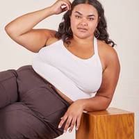 Alicia is 5'9" and wearing XL Halter Top in Vintage Off-White paired with espresso brown Western Pants. She is sitting sideways on a wooden box and her right elbow is leaning on another wooden box.