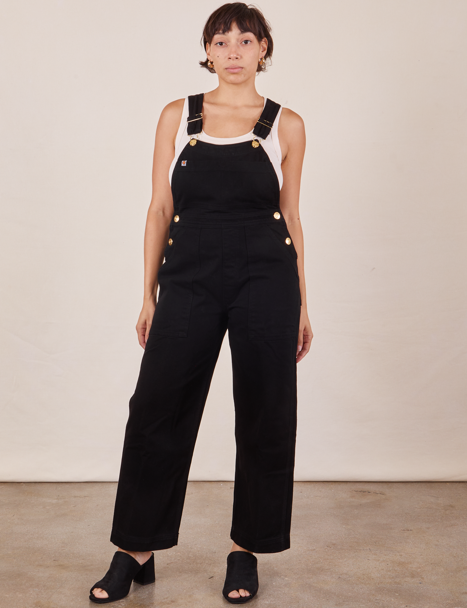 Tiara is 5'4" and wearing size XS Original Overalls in Mono Black with a Cropped Tank Top in vintage tee off-white  underneath.