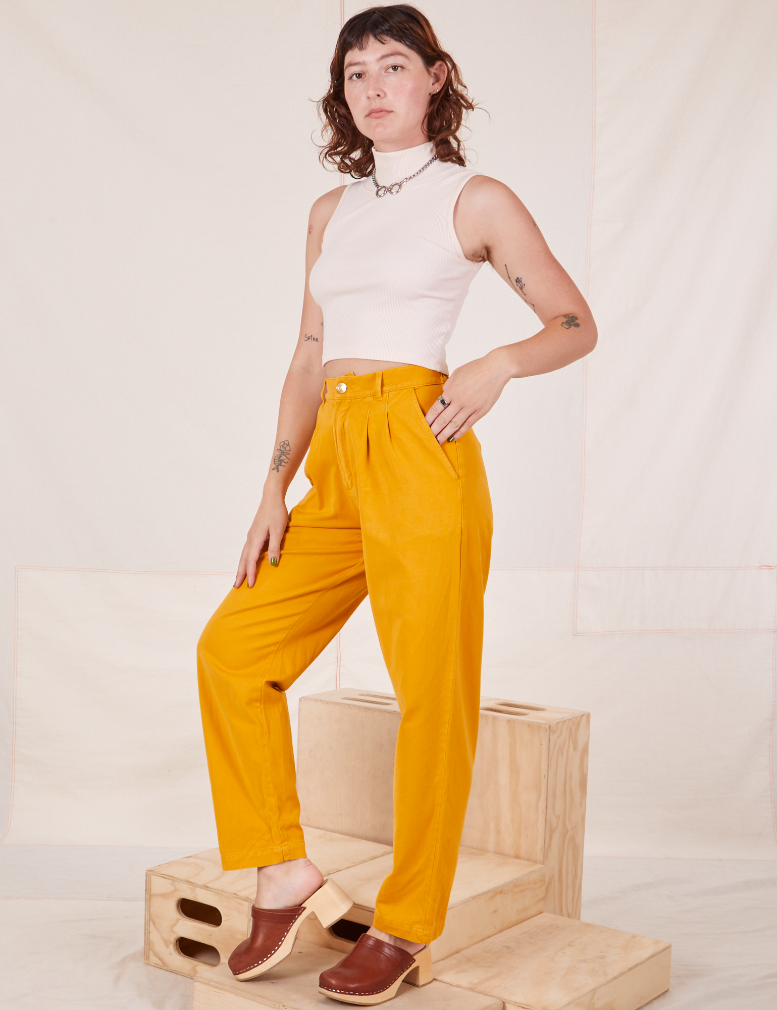 Alex is 5&#39;8&quot; and wearing XXS Organic Trousers in Mustard Yellow paired with Sleeveless Turtleneck in vintage tee off-white