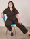 Ashley is sitting in a blue and brass chair wearing Petite Short Sleeve Jumpsuit in Espresso Brown