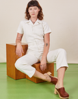 Alex is sitting on a wooden block wearing Short Sleeve Jumpsuit in Vintage Tee Off-White