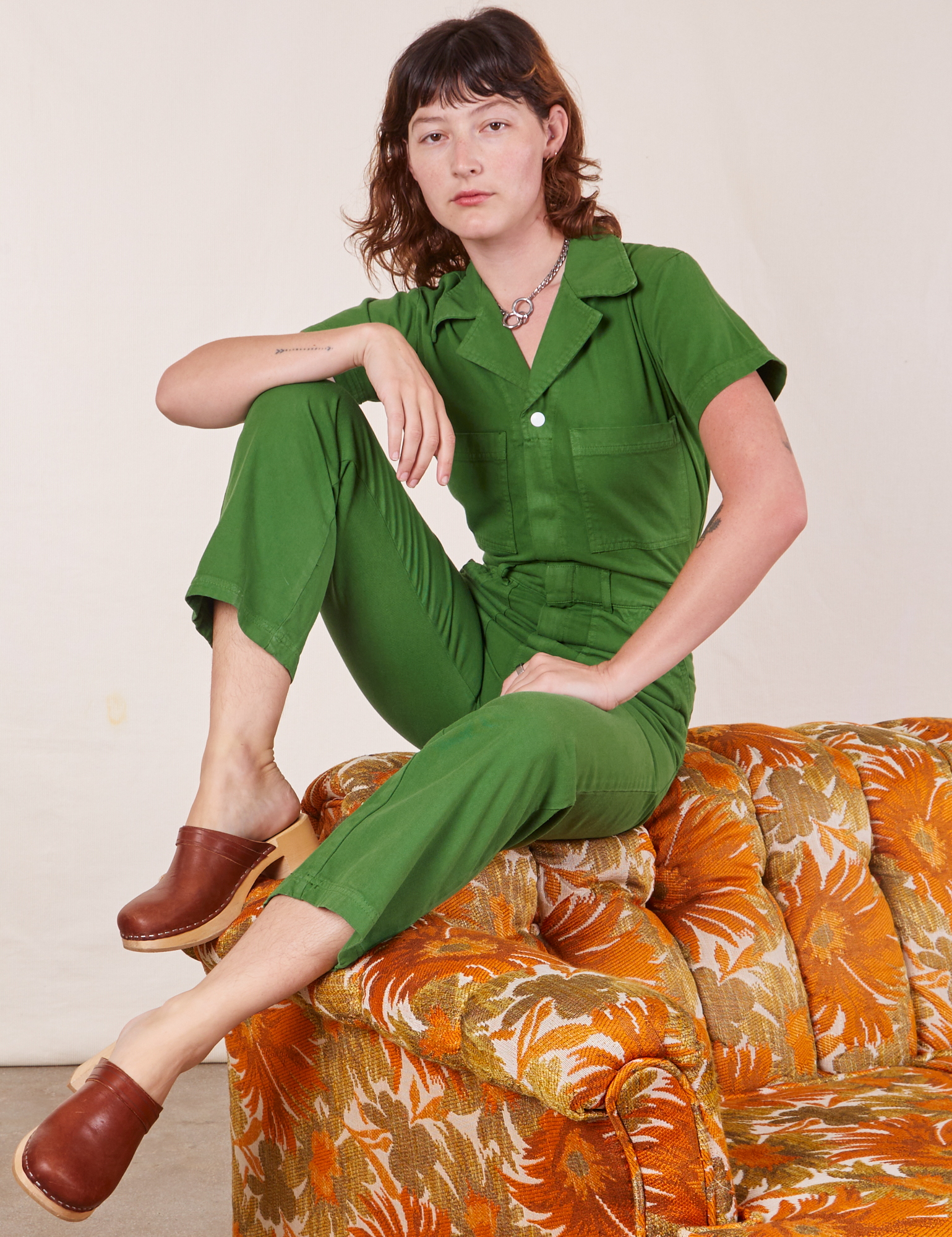 Alex is sitting on a floral couch wearing Short Sleeve Jumpsuit in Lawn Green
