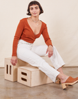 Soraya is sitting on a wooden crate wearing Work Pants in Vintage Off-White and burnt terracotta Wrap Top