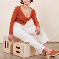 Soraya is sitting on a wooden crate wearing Work Pants in Vintage Off-White and burnt terracotta Wrap Top