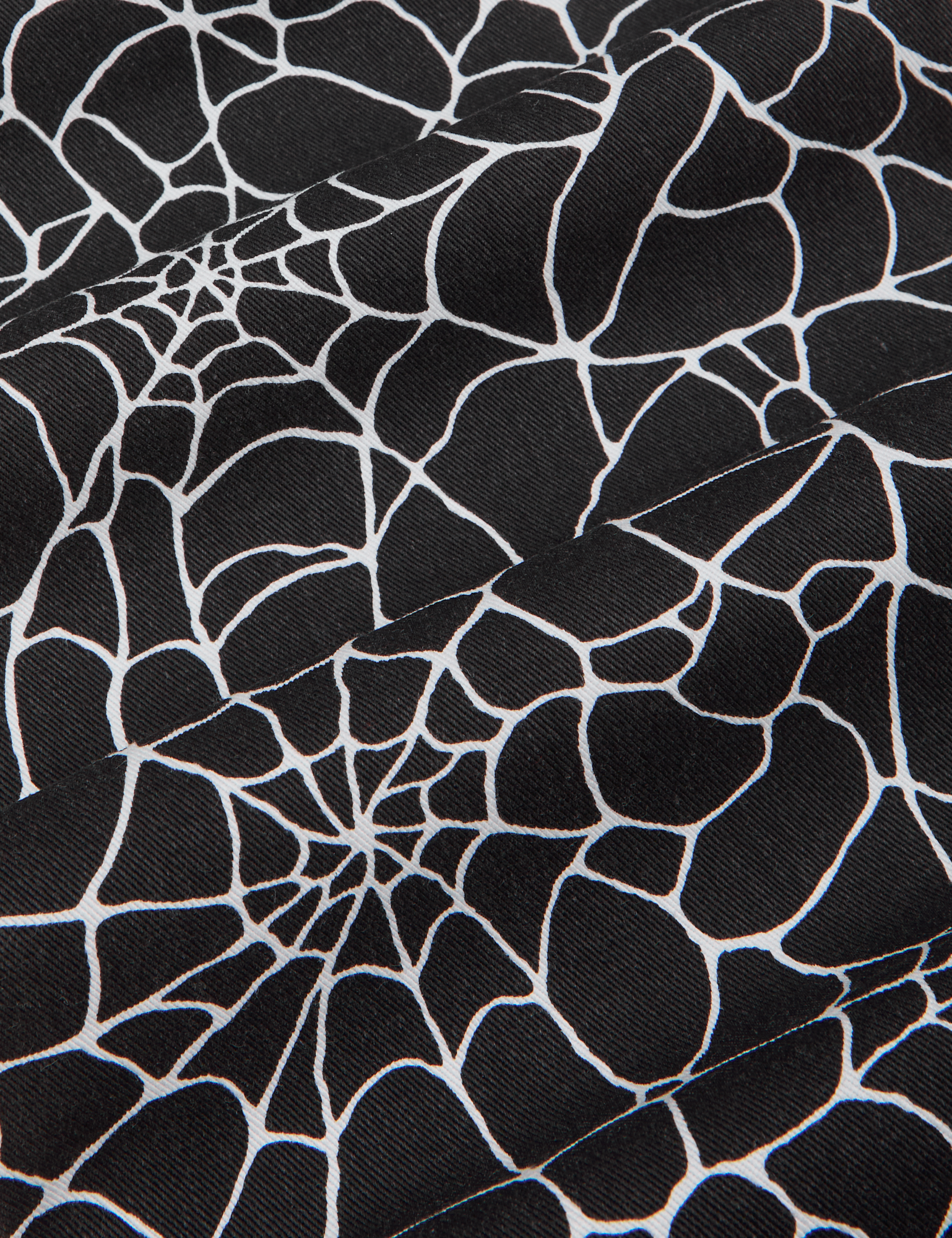 Everyday Jumpsuit in Spiderwebs fabric detail close up. Black background with white screenprinted spiderweb.