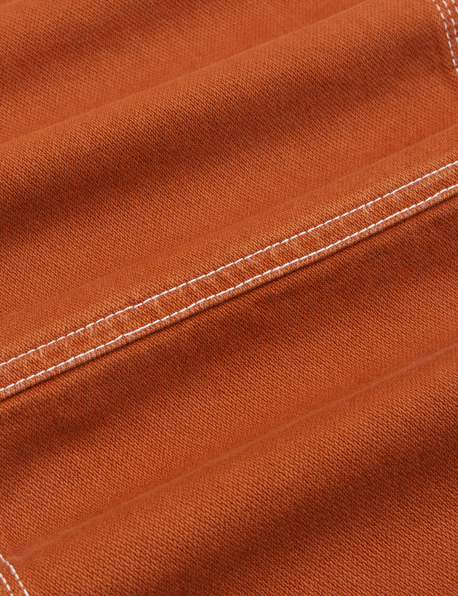 Carpenter Jeans in Burnt Terracotta fabric detail close up. Contrast white topstitching.