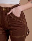 Close up of Alex's hand in the front pocket of Carpenter Jeans in Fudgesicle Brown