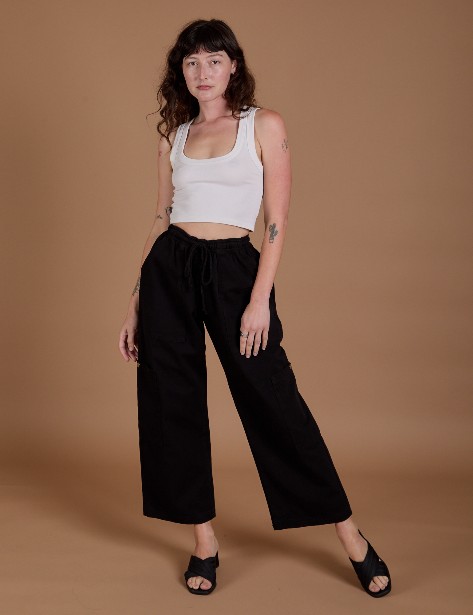 Alex is 5’8” and wearing XXS Drop Pocket Cargo Pants in Basic Black paired with a Cropped Tank in vintage tee white
