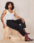 Jesse is sitting on a wooden crate wearing Heavyweight Trousers in Basic Black and Cropped Tank Top in vintage tee off-white