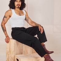 Jesse is sitting on a wooden crate wearing Heavyweight Trousers in Basic Black and vintage off-white Cropped Tank Top.