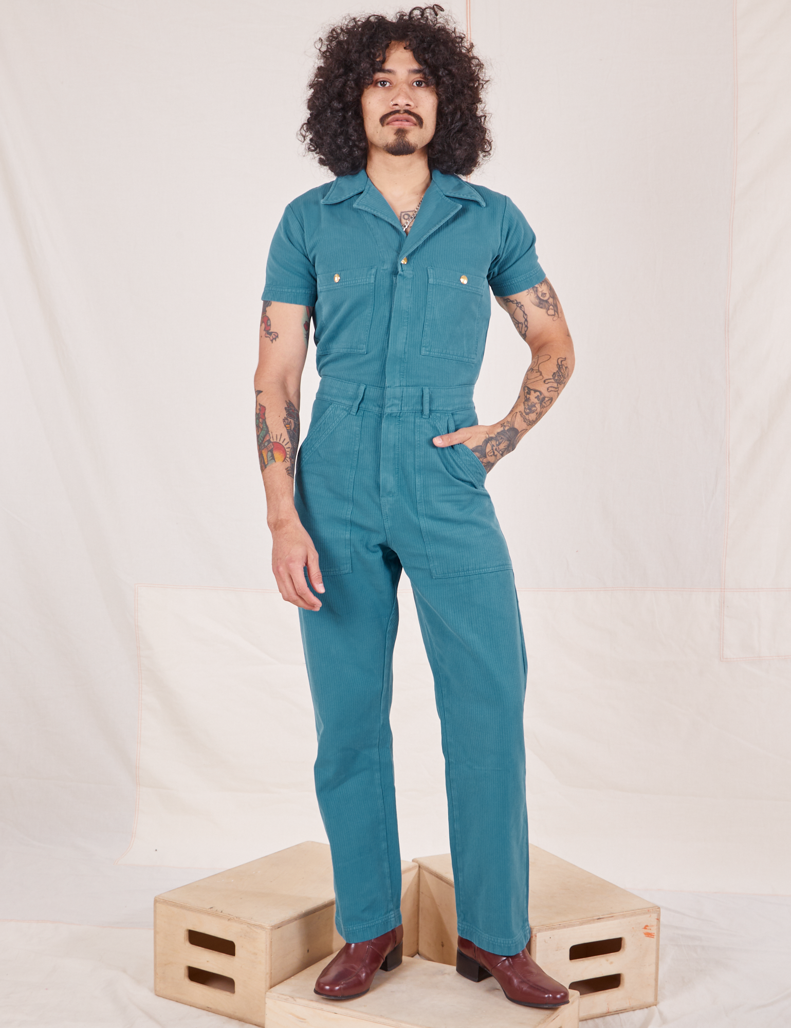 Heritage Short Sleeve Jumpsuit in Marine Blue worn by Jesse standing on wooden crate
