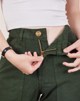 Petite Work Pants in Swamp Green front close up. Hana is pulling on the zipper tab.