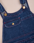 Carpenter Overalls in Dark Wash front close up. Contrast red top stitching and brass details.