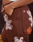 Close up of Kandia's hand in the front pocket of Gummy Bear Paintstamped Work Pants in Fudgesicle Brown