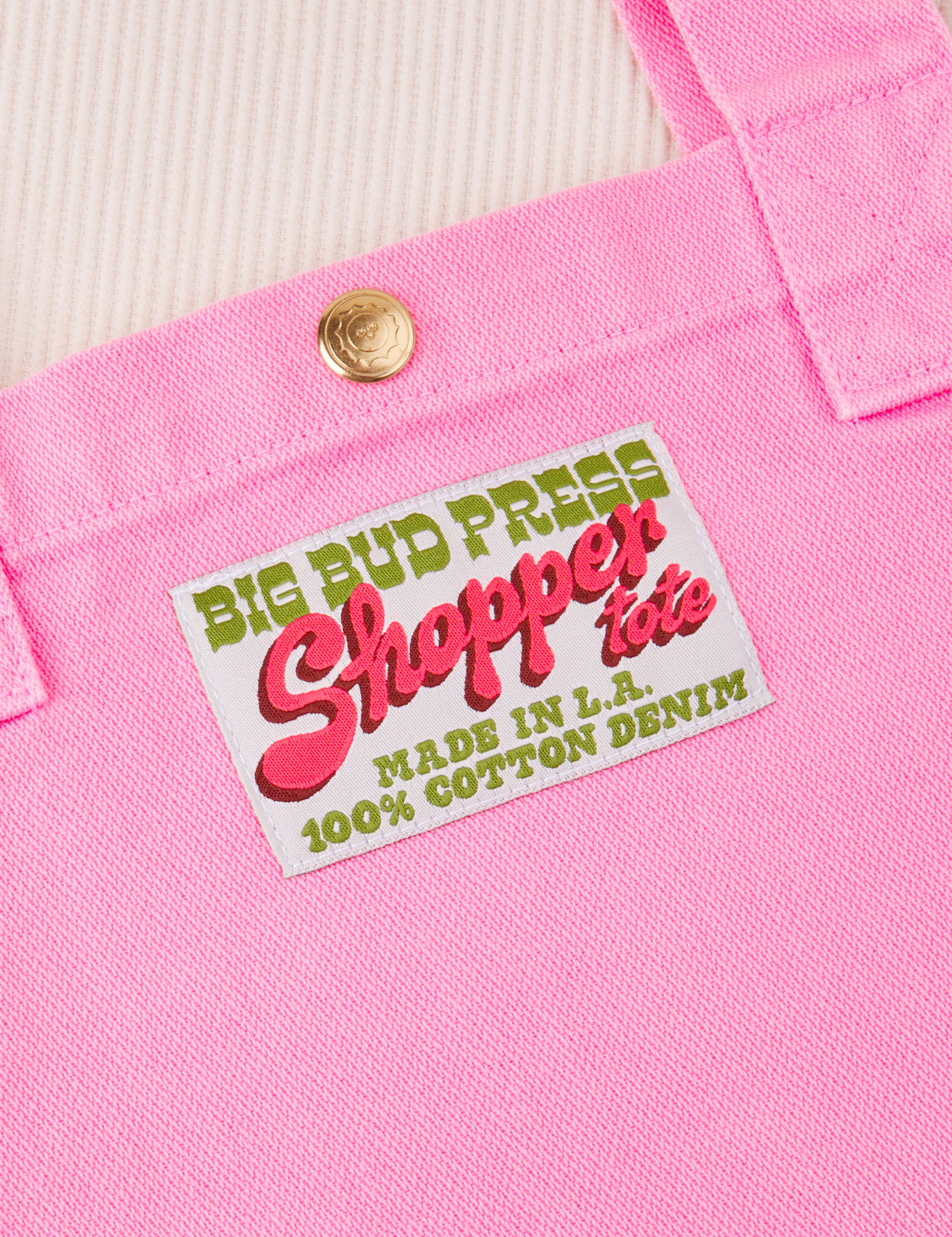 Shopper Tote Bag in Bubblegum Pink. Close up of brass sun baby snap and bag label with green and pink text on a white background