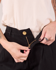 Heritage Trousers in Basic Black front close up. Alex is pulling down the zipper tab.