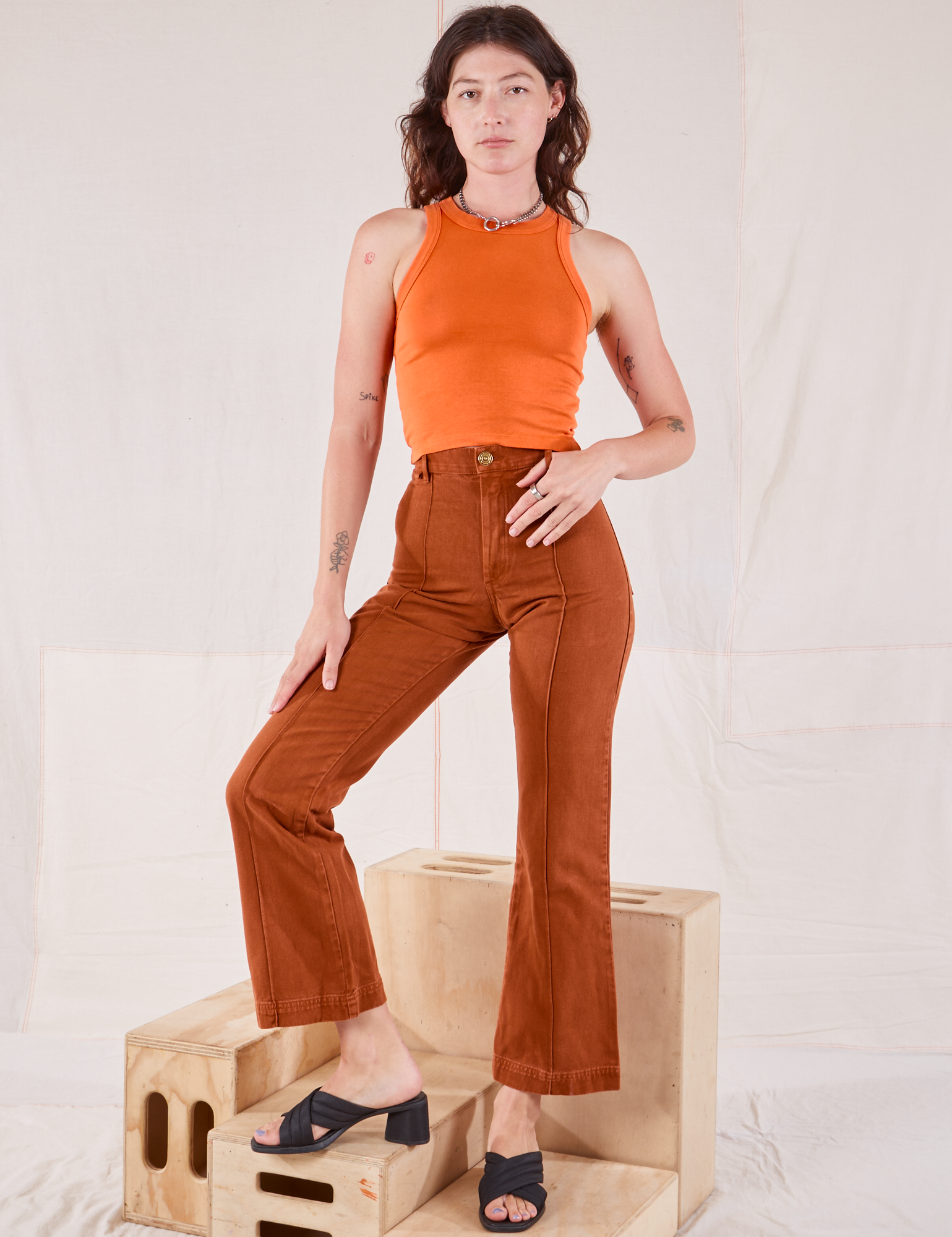 Alex is wearing Racerback Tank in Sunset Orange and burnt terracotta Western Pants