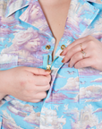 Front close up of Cloud Kingdom Jumpsuit. Ashley is holding onto the brass zipper tab.