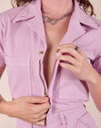 Short Sleeve Jumpsuit in Lilac front close up. Alex is pulling down the zipper.