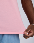 Close up of Isaac pulling on the bottom hem of Jr. Varsity Tee in Baby Pink