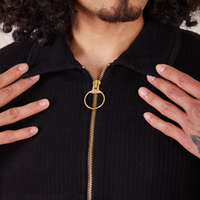 Front close up of Ricky Jacket in Basic Black. Jesse has both hands on each collar point. Brass zipper and ring pull along the front of the jacket.