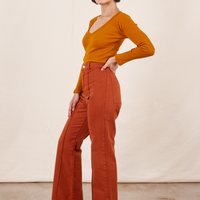 Side view of Western Pants in Burnt Terracotta paired with a burnt orange Long Sleeve V-Neck Tee worn by Soraya