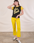 Alex is wearing Anniversary Tee in I’m Tired paired with golden yellow Work Pants