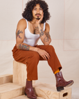 Jesse is sitting on a wooden crate. They are wearing Heavyweight Trousers in Burnt Terracotta and Cropped Cami in vintage tee off-white