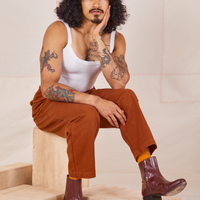 Jesse is sitting on a wooden crate. They are wearing Heavyweight Trousers in Burnt Terracotta and vintage off-white Cropped Cami.