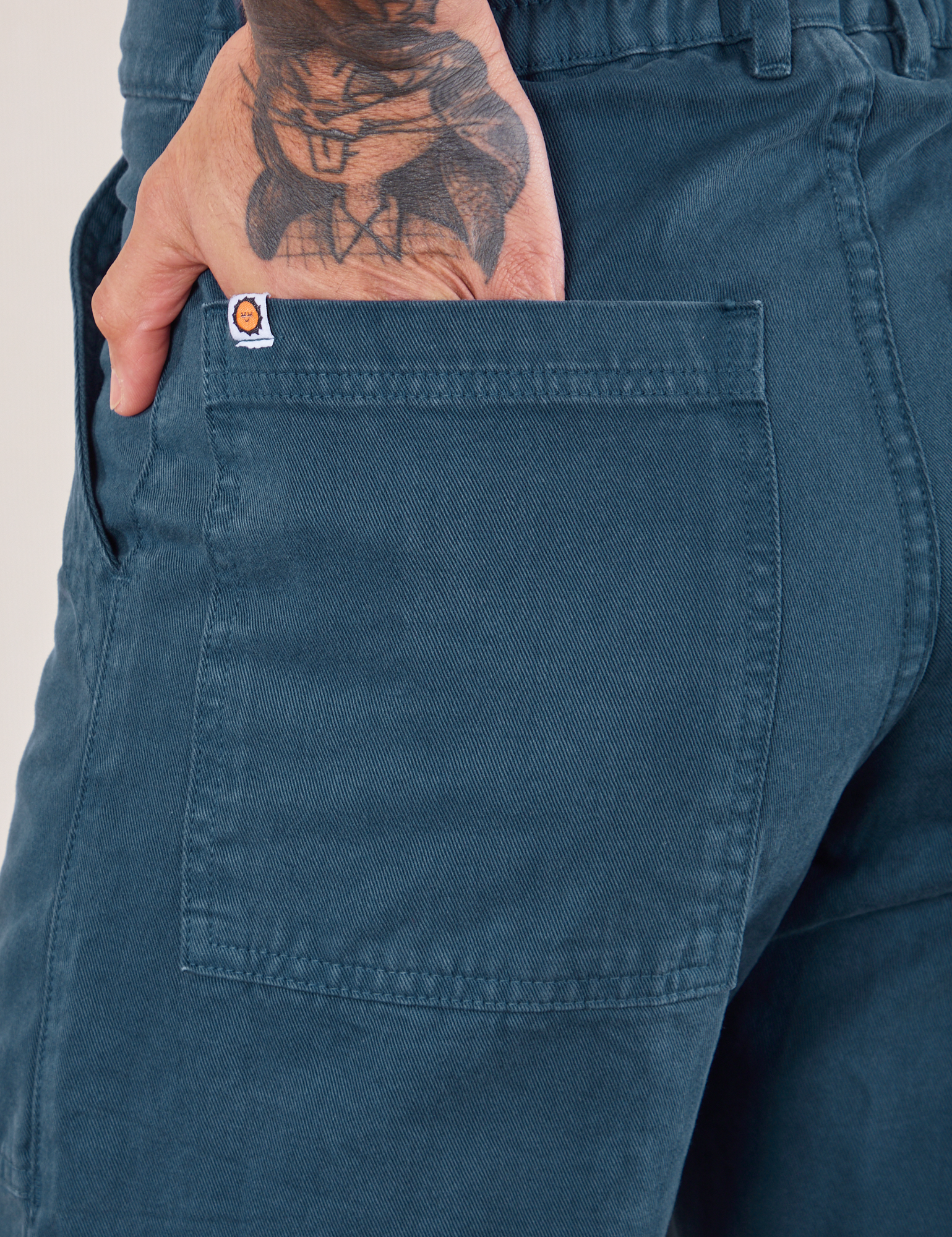 Work Pants in Lagoon back pocket close up. Jesse has their hand in the pocket.