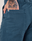 Work Pants in Lagoon back pocket close up. Jesse has their hand in the pocket.