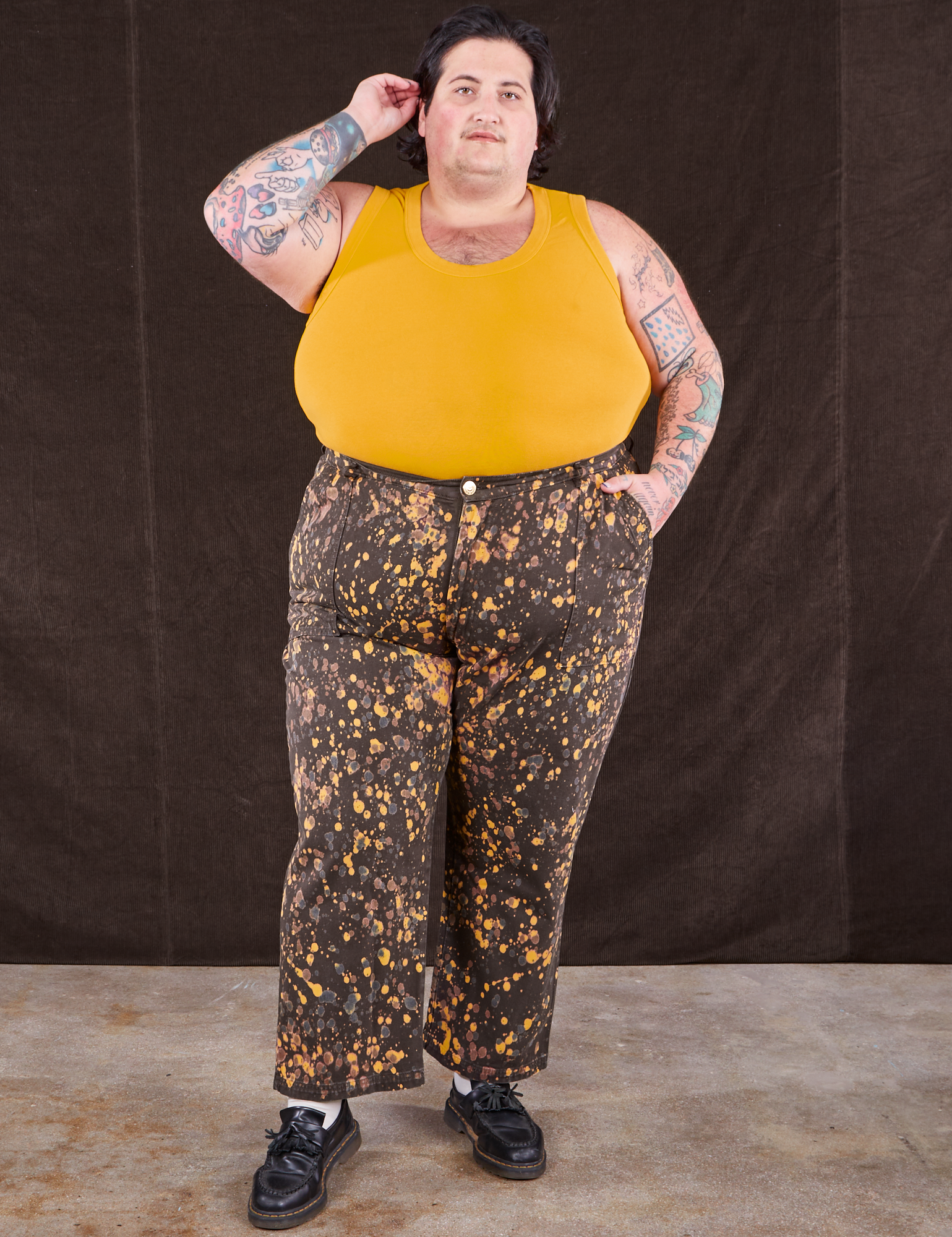 Sam is wearing Marble Splatter Work Pants in Espresso Brown and mustard yellow Tank Top