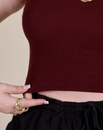Close up of Sydney holding the bottom hem of Muscle Tee in Red Wine
