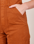 Front pocket close up of Short Sleeve Jumpsuit in Burnt Terracotta. Alex has her hand in the pocket