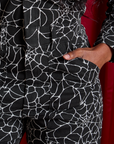 Close up of Kandia's hand in the front pocket of Everyday Jumpsuit in Spiderwebs