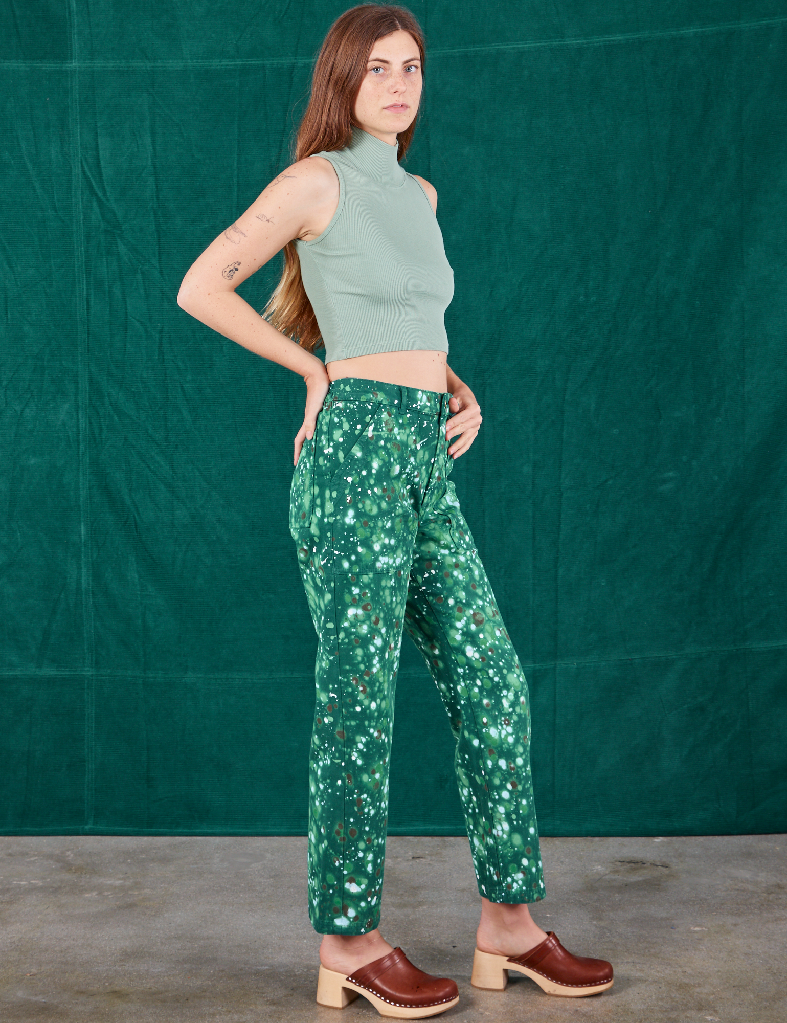 Side view of Marble Splatter Work Pants in Hunter Green and sage green Sleeveless Turtleneck worn by Scarlett