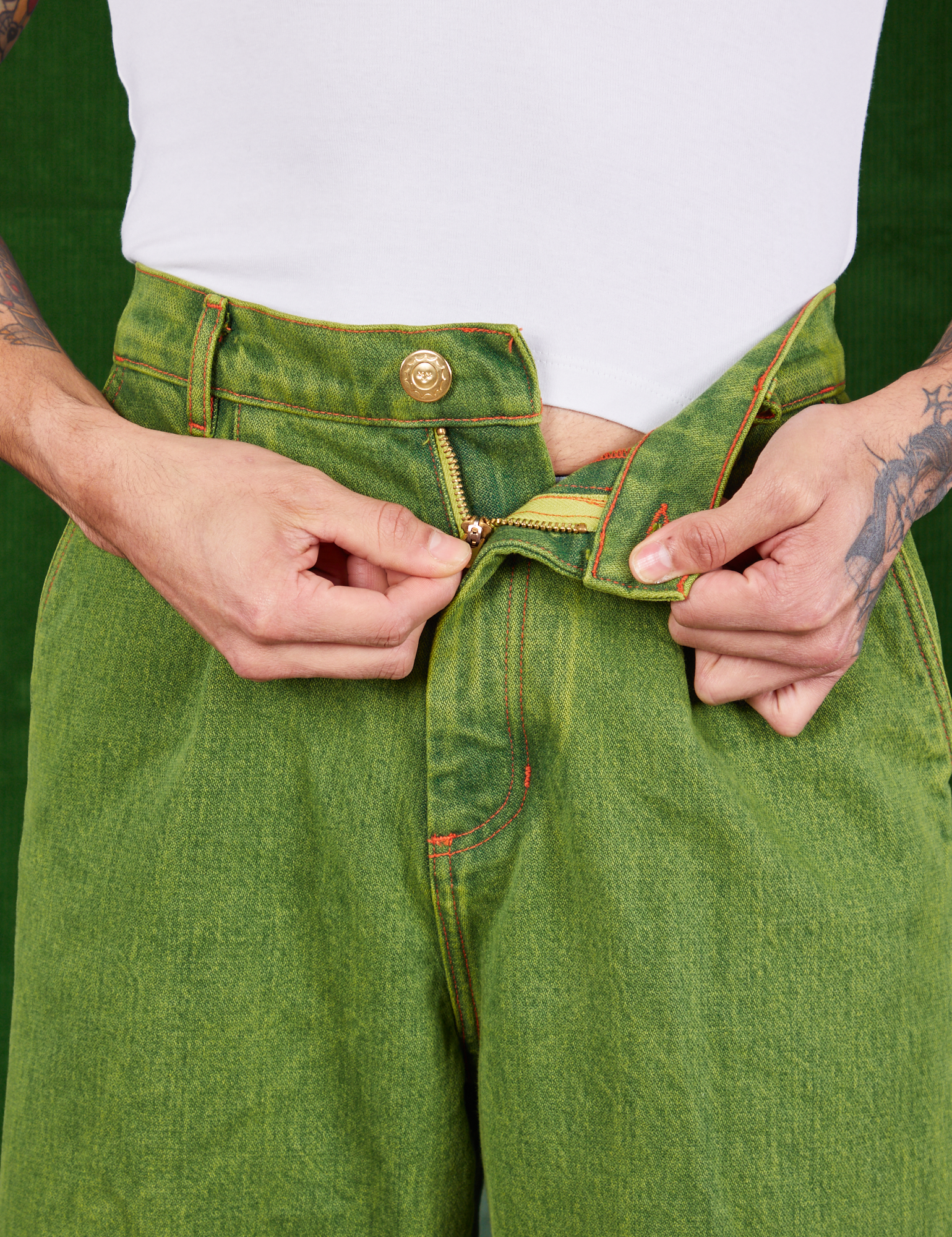 Front close up of Overdyed Wide Leg Trousers in Gross Green. Jesse is pulling on the zipper tab