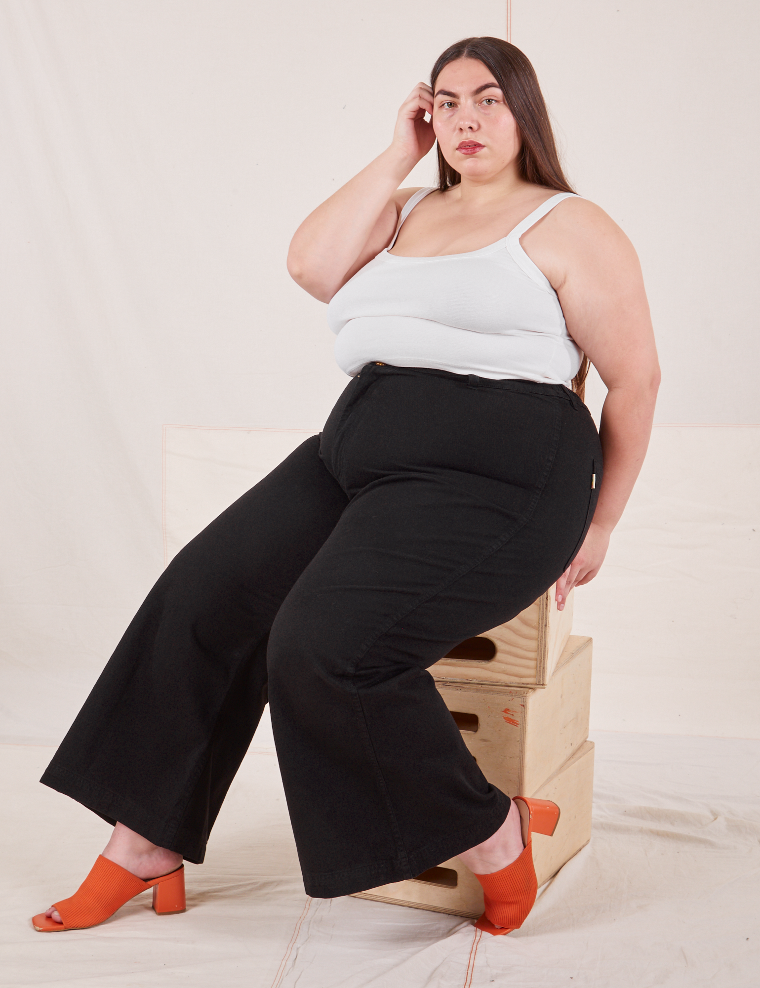 Marielena is wearing Bell Bottoms in Basic Black and Cropped Cami in vintage tee off-white. She is sitting on a stack of wooden crates.