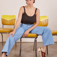 Tiara is sitting on vinyl dining chairs wearing Cropped Cami in Espresso Brown and light wash Sailor Jeans