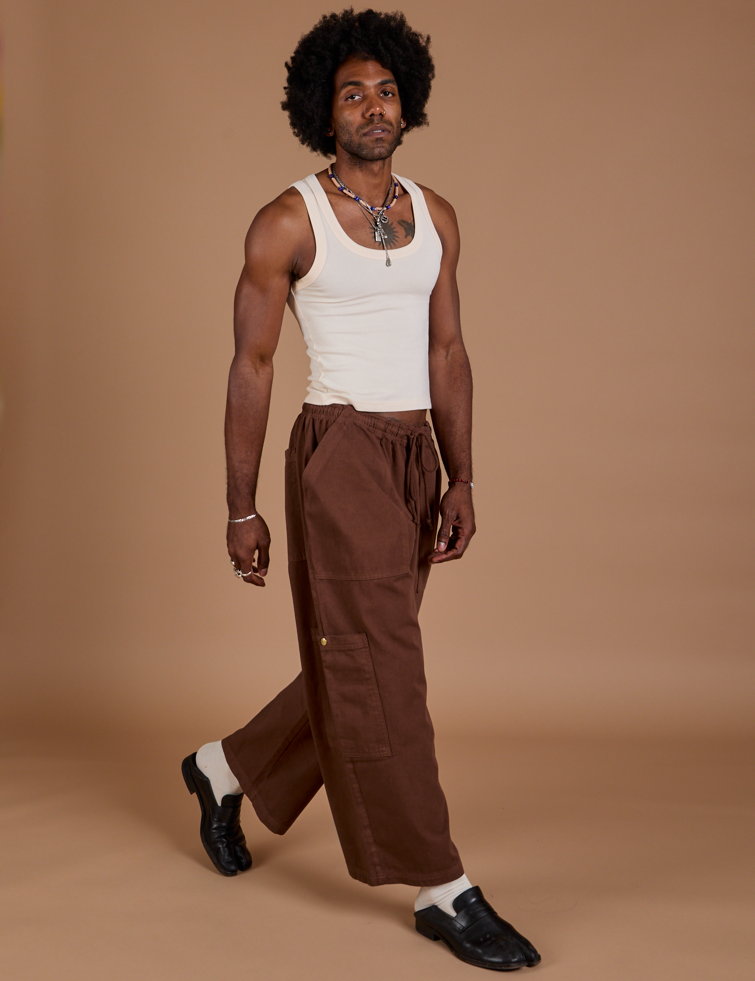 Angled front view of Drop Pocket Cargo Pants in Fudgesicle Brown and Tank Top in vintage tee white on Jerrod