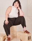 Ashley is sitting on a wooden crate wearing Heavyweight Trousers in Espresso Brown and Sleeveless Turtleneck in vintage tee off-white