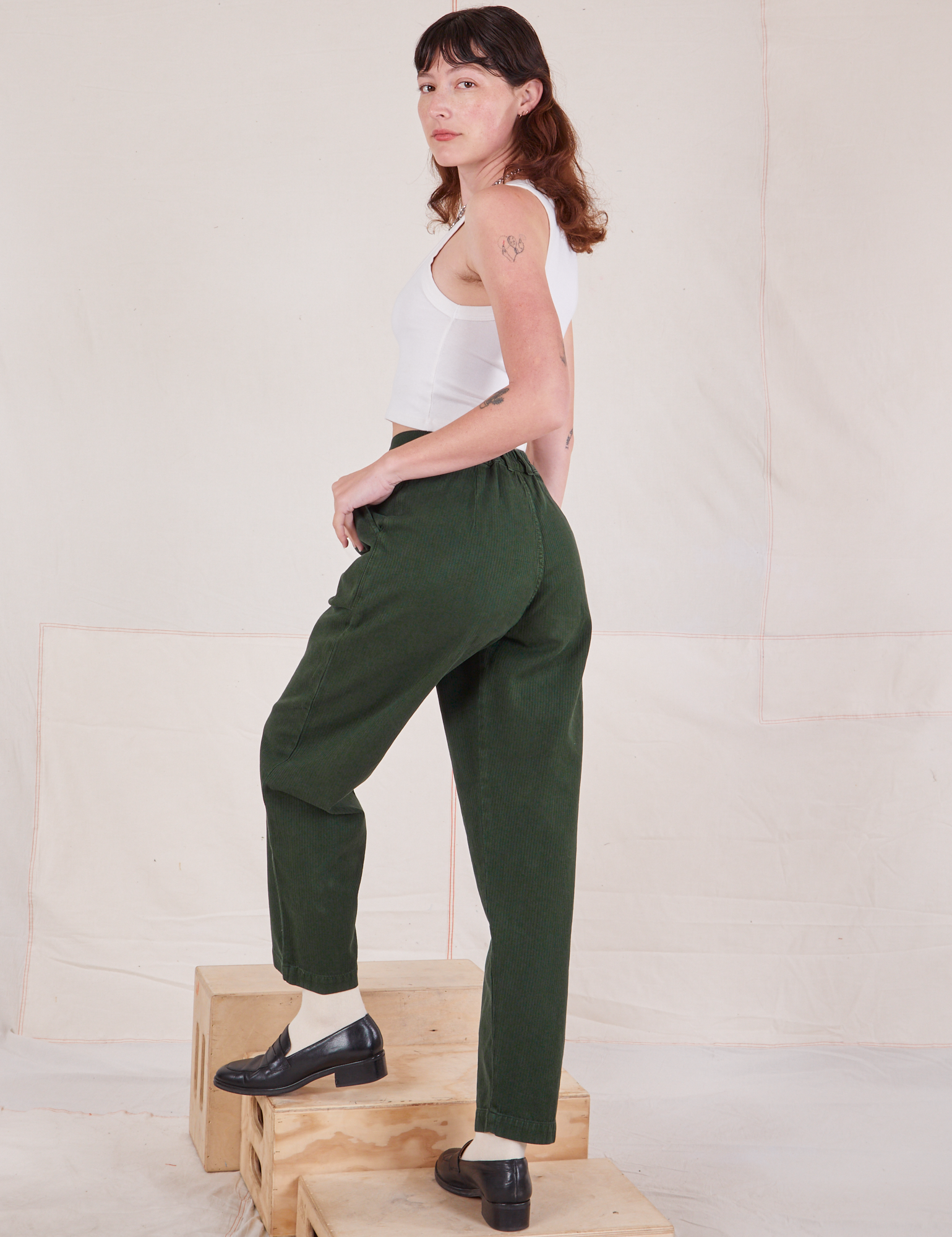 Angled back view of Heritage Trousers in Swamp Green and Cropped Tank Top in vintage tee off-white on Alex