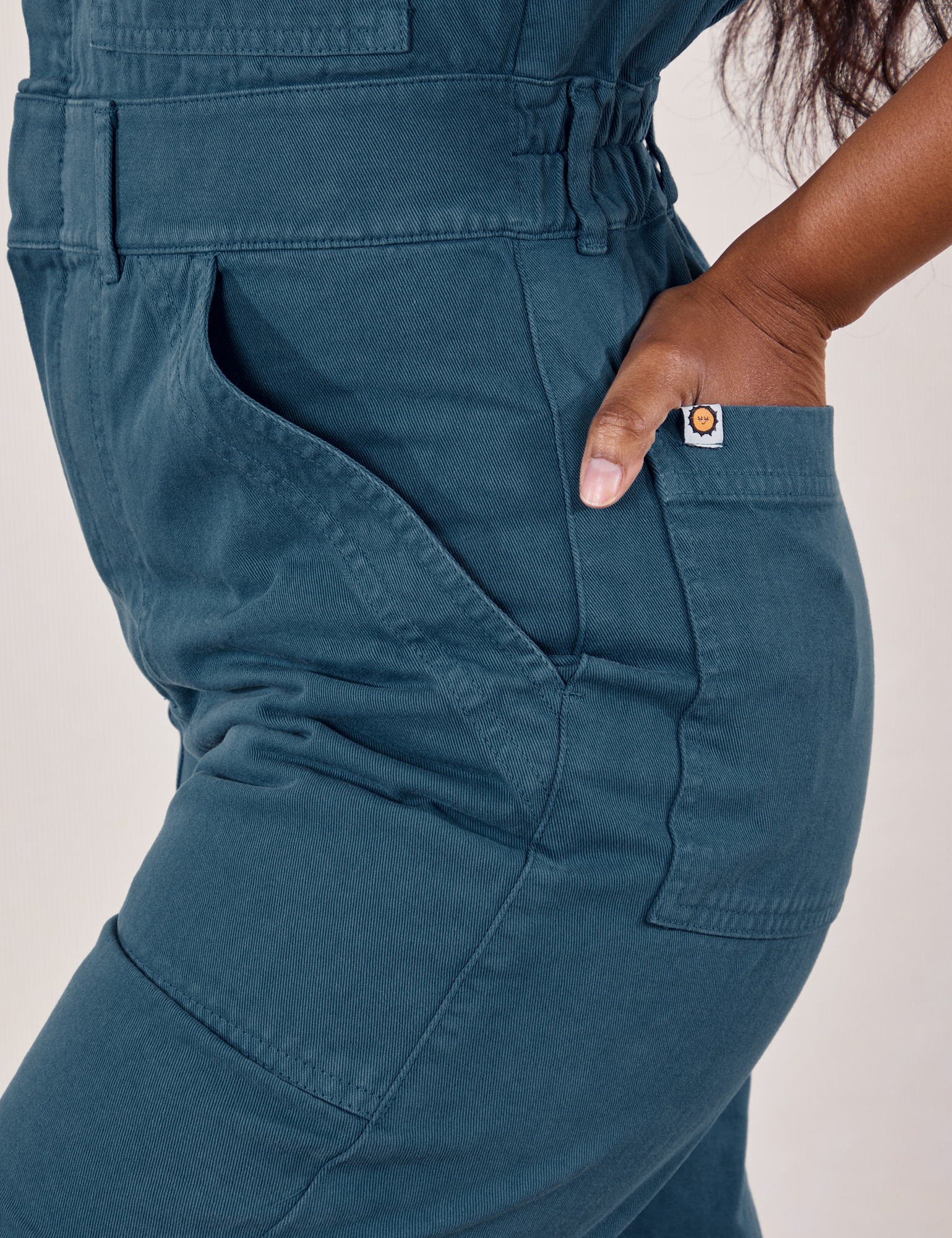 Petite Short Sleeve Jumpsuit in Lagoon side close up. Kandia has her hand in the back pocket.